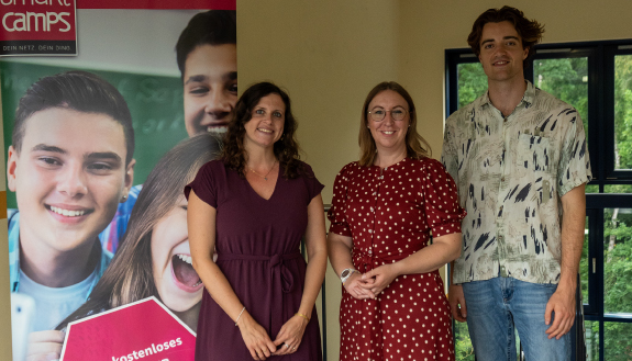 Smart Camp - Zwei Frauen in Kleidern und ein Mann stehen nebeneinander