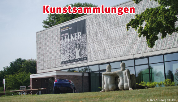 Das Bild zeigt die Kunsthalle in Rostock von außen. Vor der Kunsthalle ist eine Grünfläche mit Bäumen zu sehen. Auf der Grünfläche befindet sich eine Statue mit zwei Menschen.