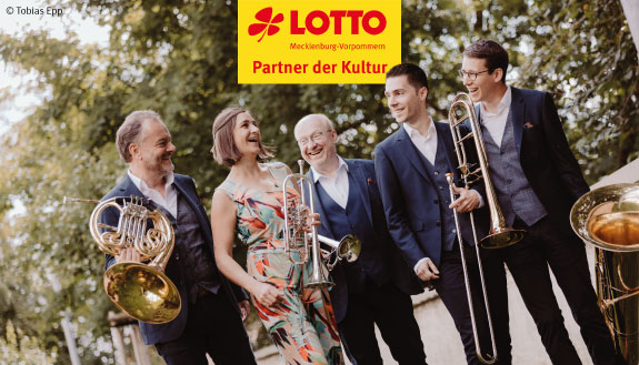 Das Quintett Harmonic Brass steht mit Ihren Musikinstrumenten. Im Hintergrund sind Bäume zu sehen.