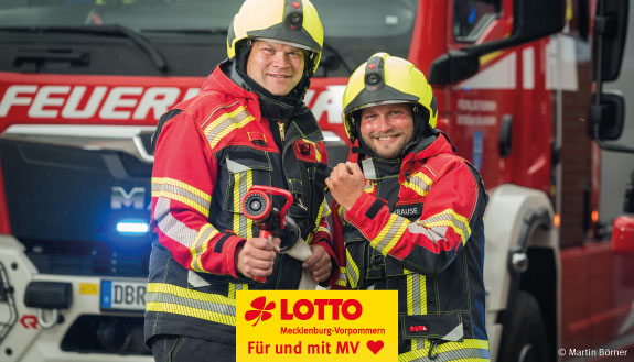 Oberlöschmeister Tim Nahrstedt steht gemeinsam mit Kollegen vor Feuerwehrauto