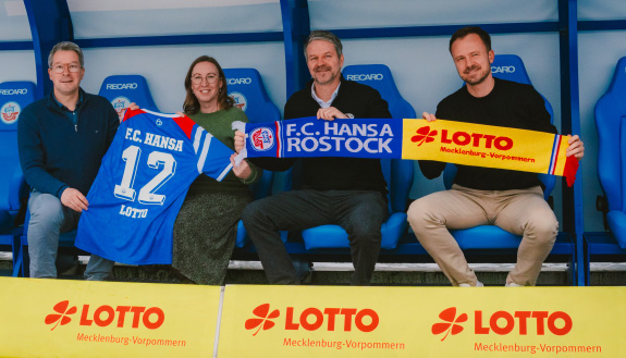 Vier Personen zeigen Trikot und Schal mit Schriftzug bzw. Logo von FCH und LOTTO MV