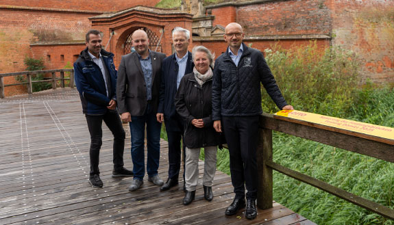 Landrat Stefan Sternberg und Geschäftsführer von LOTTO-Mecklenburg-Vorpommern, Hubert Ludwig, gemeinsam mit dem Förderkreis Festung Dömitz e. V. stehen auf der neuen Festungsbrücke von Dömitz.