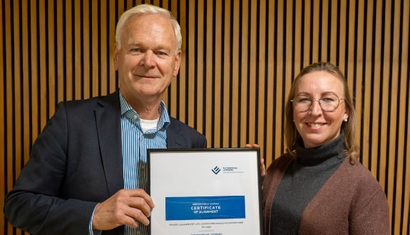 Das Bild zeigt zwei Personen, einen Mann und eine Frau. Die zwei Personen halten gemeinsam ein Zertifikat in der Hand.