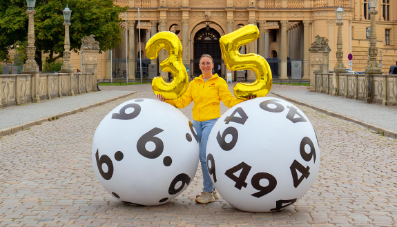 Frau steht mit 35-Luftballon zwischen zwei gro&szlig;en LOTTO-Kugeln